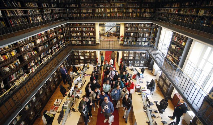 Visitantes recorriendo los espacios de trabajo de la Biblioteca con estanterías de libros a la vista.