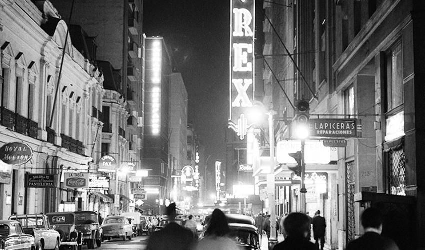 personas caminando por una calle antiguedad de Santiago, imagen en blanco y negro, antigua, destacan las luces de las marquesinas y de la ciudad.